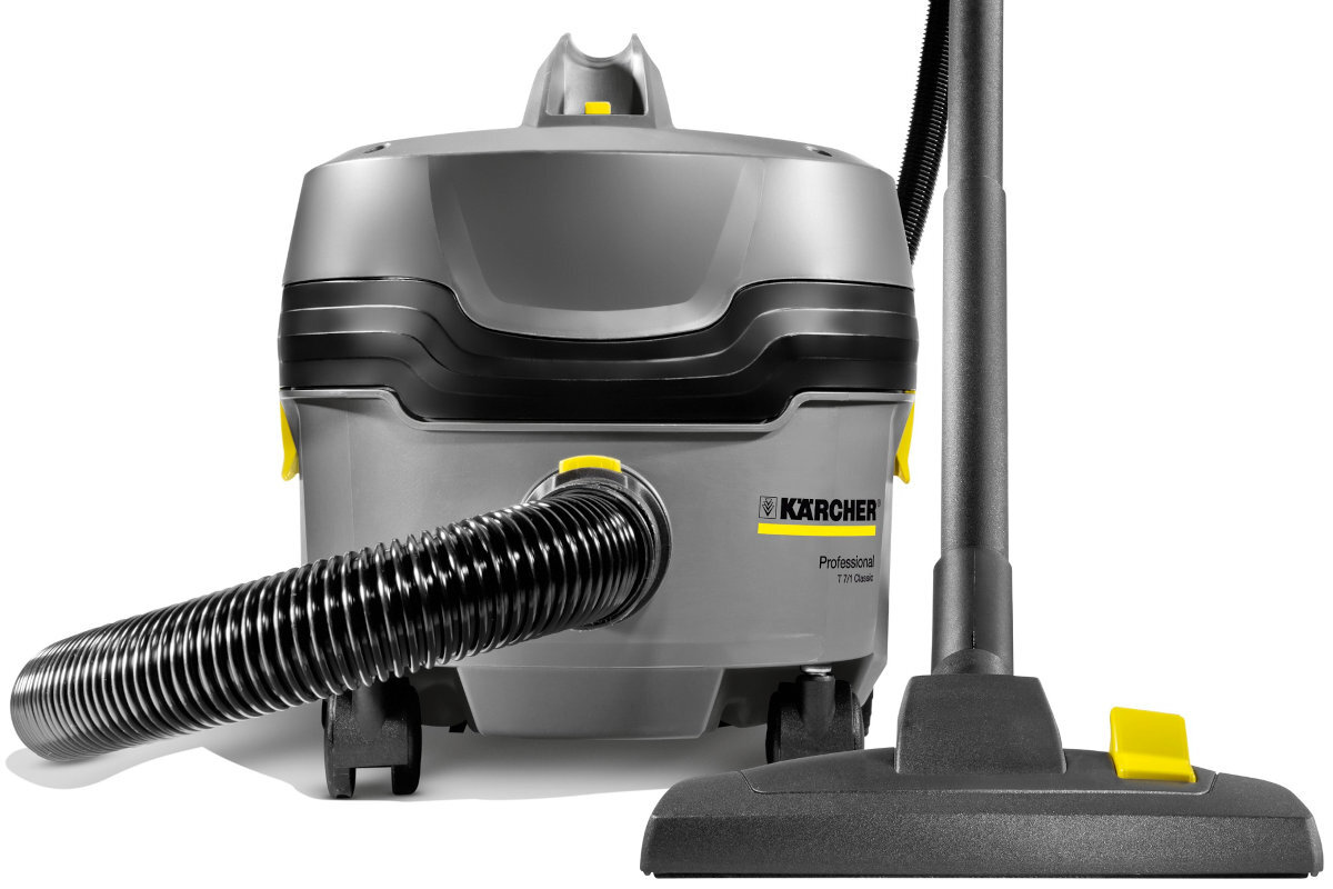 Na obrazie widoczny jest szary odkurzacz przemysłowy z czarnym wężem i żółtymi elementami. Na urządzeniu znajduje się logo \'KARCHER\' oraz napis \'Professional T 7/1 Classic\'.