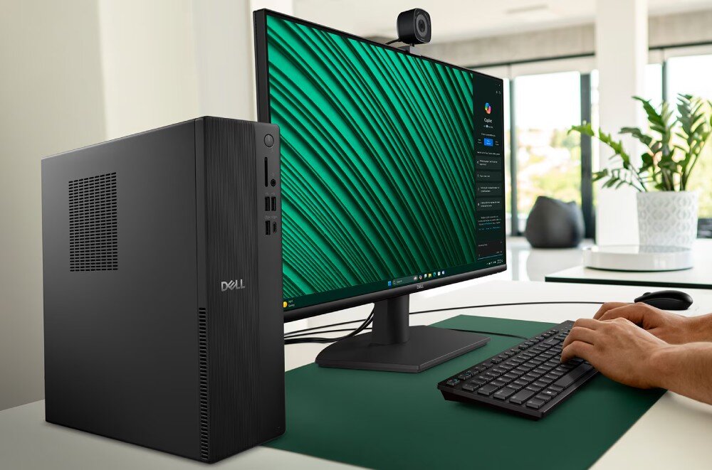Komputer DELL Slim ECS1250 osoba pisze na czarnej klawiaturze przy komputerze stacjonarnym w wąskiej obudowie, obok którego stoi monitor z kolorową grafiką i kamerką internetową na górnej krawędzi, opis