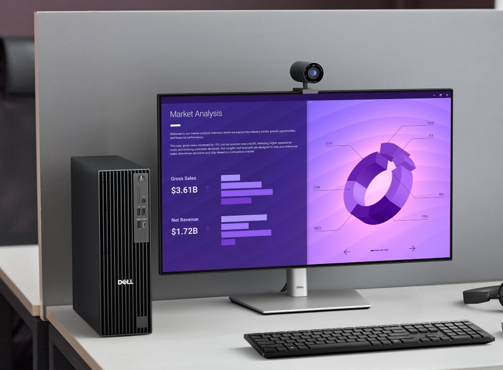 Komputer DELL Pro Slim Plus QBS1250 Komputer stacjonarny w czarnej obudowie typu slim stoi pionowo na białym biurku obok monitora wyświetlającego fioletowe wykresy analizy rynku, opis