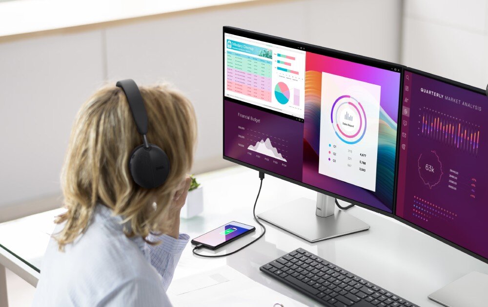 Komputer DELL Pro Slim Plus QBS1250 Kobieta w słuchawkach siedząca tyłem przy biurku z dwoma monitorami, na których widoczne są kolorowe panele z danymi finansowymi i wykresami, porty, łączność bezprzewodowa