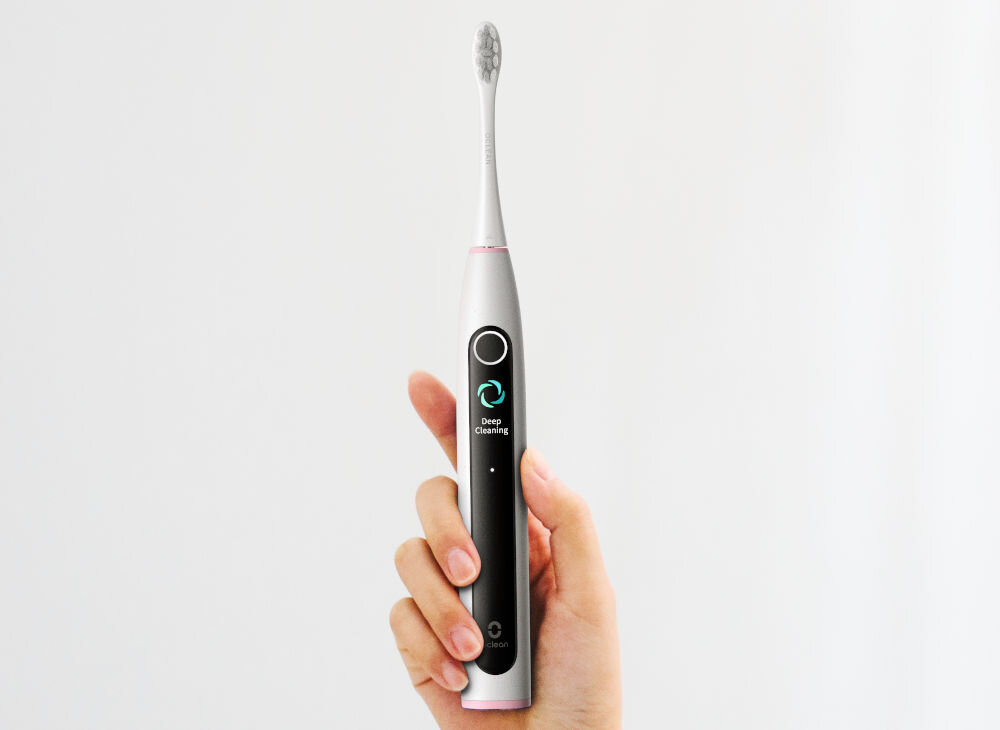 Osoba trzyma szarą szczoteczkę soniczną z wyświetlaczem, na którym widoczny jest napis \'Deep Cleaning\'.