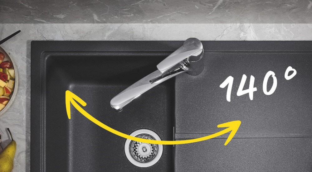 Zlewozmywak jednokomorowy z ociekaczem GROHE K200 31565SD1 Stal szlachetna Na zdjęciu przedstawiono wysoką, łukową baterię kuchenną GROHE o lśniącym chromowanym wykończeniu, zamontowaną przy stalowym zlewozmywaku na drewnianym blacie. Na ociekaczu leżą zielone papryczki, a w tle widać płytę grzewczą i drewniane młynki do przypraw na tle jasnej, pastelowej ściany wysoka wylewka bateria obracana 360° elastyczność kuchnia napełnianie garnków mycie naczyń komfort użytkowania duże garnki