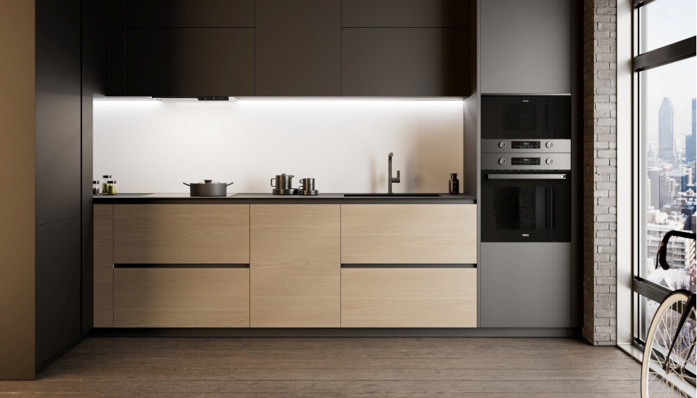 Piekarnik TEKA NEO HSB 6350 SS Zdjęcie przedstawia jasną, minimalistyczną kuchnię z zabudowanym piekarnikiem i kuchenką mikrofalową TEKA umieszczonymi po prawej stronie. Całość utrzymana jest w beżowo‑kremowej kolorystyce z drewnianymi akcentami i dużymi przeszkleniami zapewniającymi widok na miasto