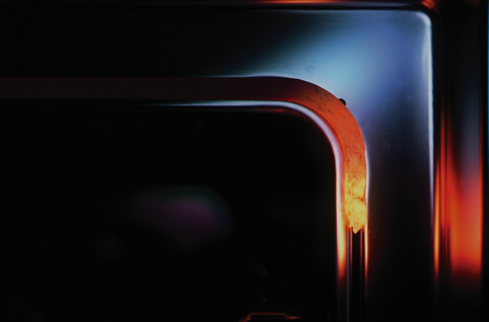 Piekarnik TEKA NEO HSB 6350 SS Zdjęcie przedstawia zbliżenie na zaokrągloną, metaliczną krawędź urządzenia, oświetloną intensywnymi czerwonymi i niebieskimi refleksami. Kontrast barw podkreśla formę i wysoką jakość wykończenia materiału energooszczędny piekarnik szczelność temperatura precyzja wypieki System ThermoSeal