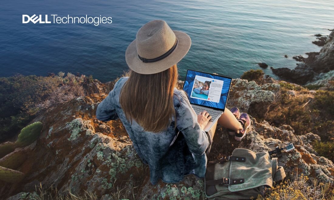 Osoba siedzi na skalistym brzegu z laptopem na kolanach, patrząc na ekran. W lewym górnym rogu widoczne jest logo \'DELL Technologies\'.