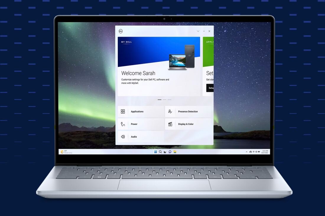 Laptop z otwartym ekranem, na którym wyświetlana jest aplikacja z tekstem \'Welcome Sarah\'. W tle widoczny jest krajobraz z zorzą polarną.