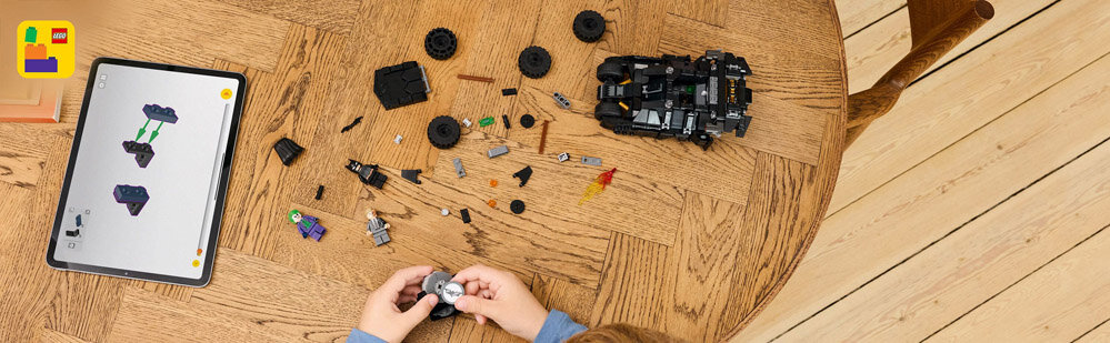 Na drewnianym stole leżą rozłożone elementy zestawu LEGO oraz złożony model pojazdu. Obok znajduje się tablet z instrukcją budowy LEGO.