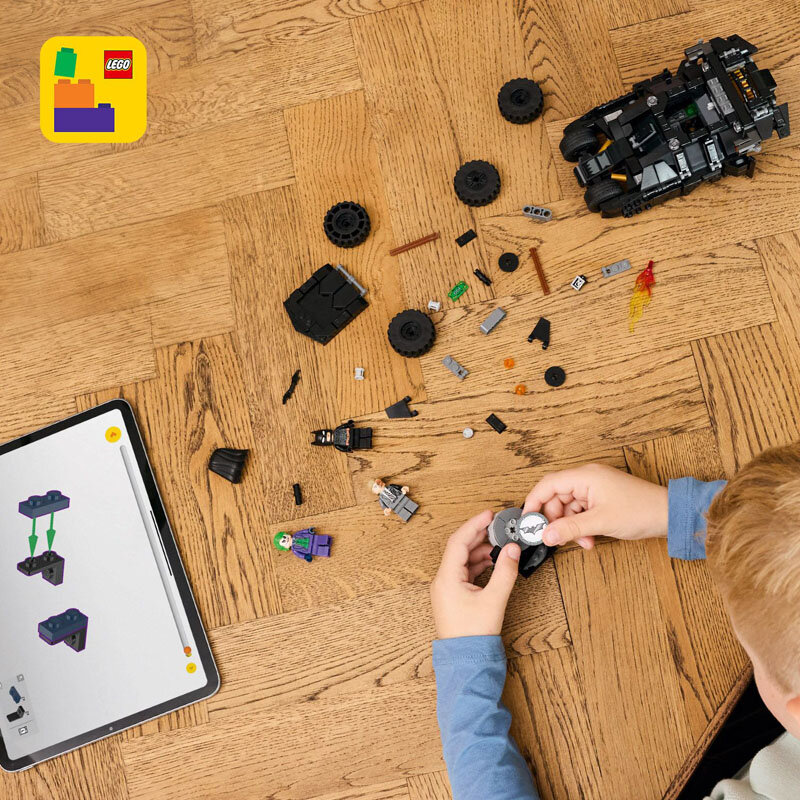 Na drewnianej podłodze leżą rozłożone elementy zestawu LEGO, w tym figurki i części pojazdu. Obok znajduje się tablet z instrukcją budowy, a w rogu widoczne jest logo LEGO.