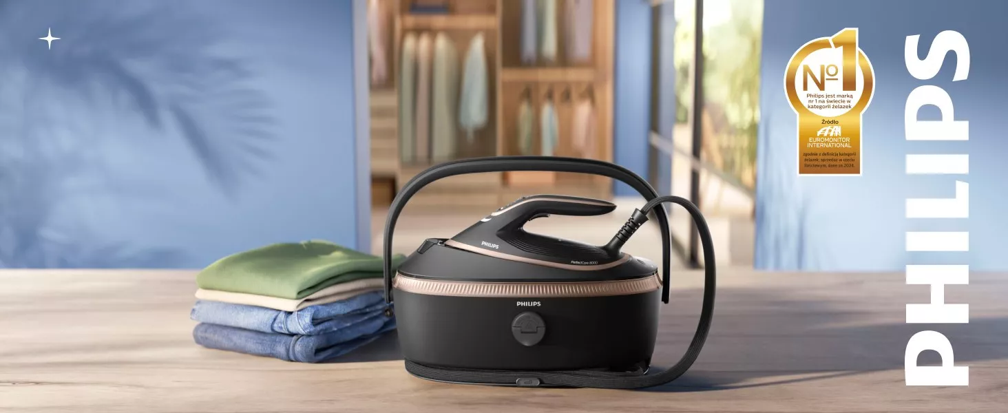 Na drewnianym stole znajduje się generator pary marki PHILIPS obok stosu złożonych ubrań. W tle widoczna jest szafa z ubraniami oraz złoty emblemat z napisem \'Nr 1 Philips jest marką nr 1 na świecie w kategorii żelazek\'.