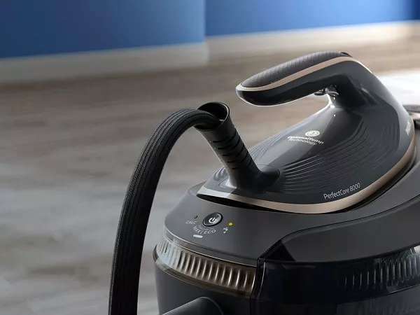 Na obrazie widoczny jest generator pary z napisem \'PerfectCare 8000\' oraz logo producenta. Urządzenie ma ciemny kolor z jasnymi akcentami i widoczny jest wąż parowy.