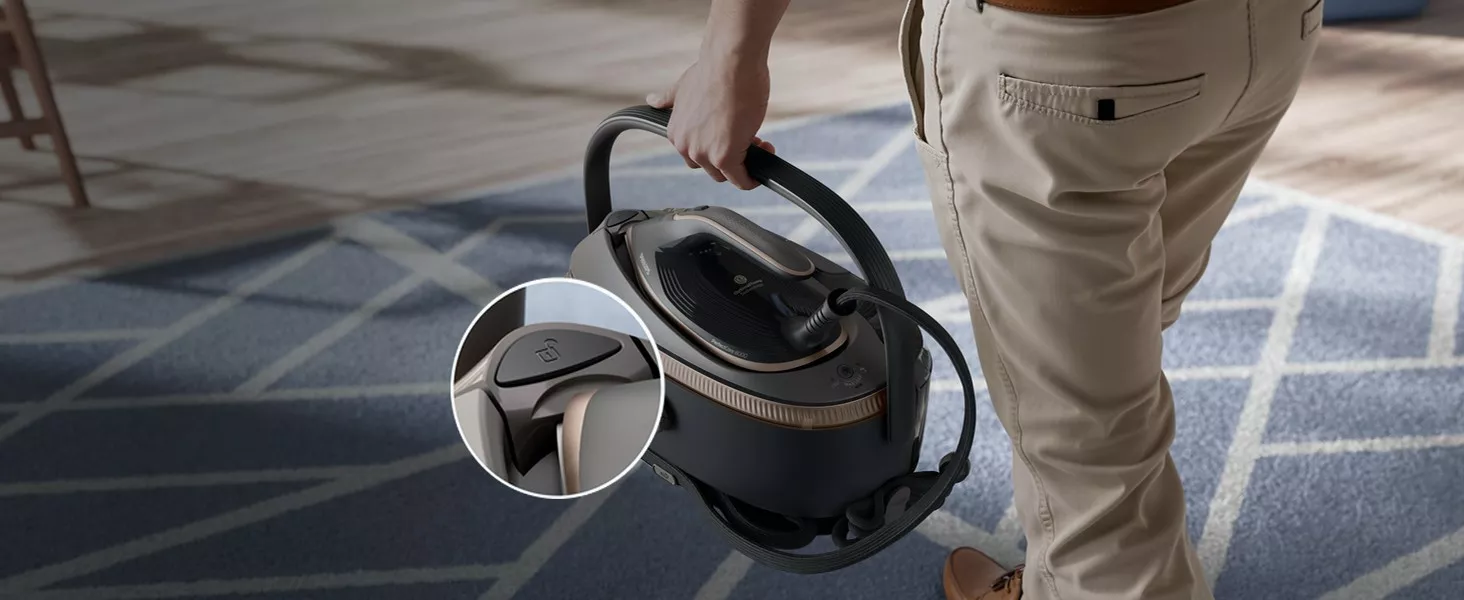 Osoba trzyma urządzenie przypominające generator pary z uchwytem, na tle dywanu z geometrycznym wzorem. W okrągłym zbliżeniu widoczny jest przycisk z symbolem kłódki.