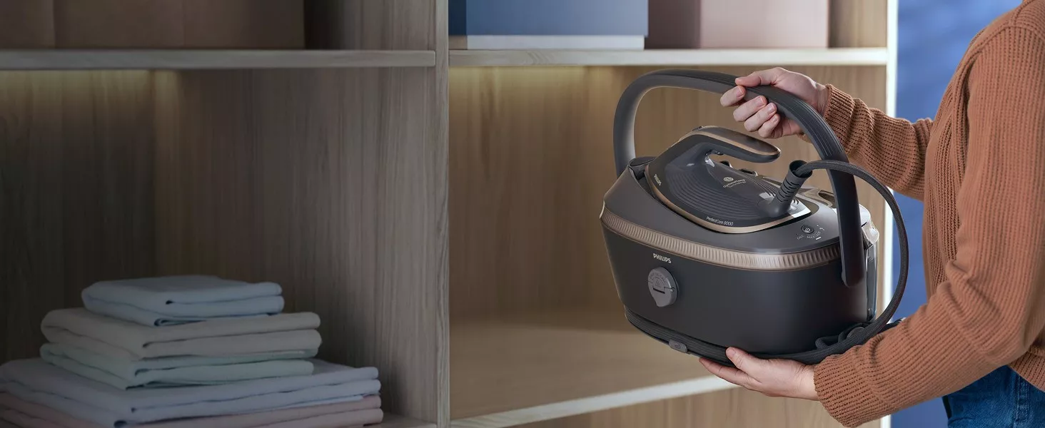 Osoba trzyma generator pary z widocznym logo \'PHILIPS\'. W tle znajduje się półka z ułożonymi ręcznikami.