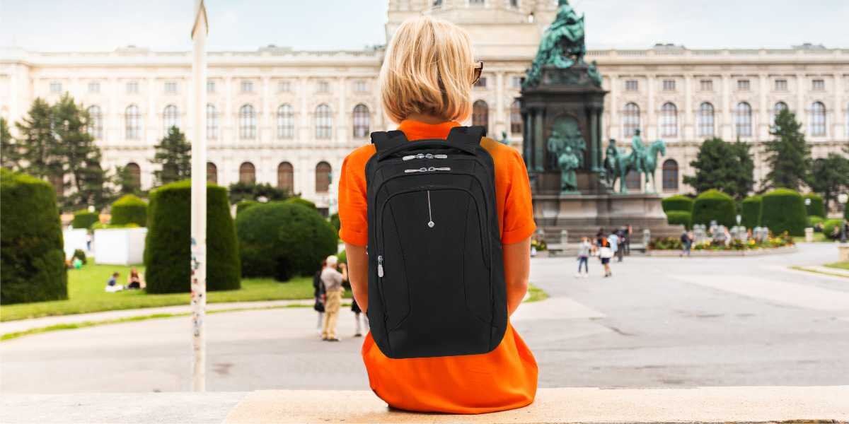 Plecak na laptopa SAMSONITE Guardit Classy 2.0 15.6 cali Czarny Kobieta z czarnym plecakiem biznesowym na plecach, siedząca przodem do zabytkowego pomnika w Wiedniu.