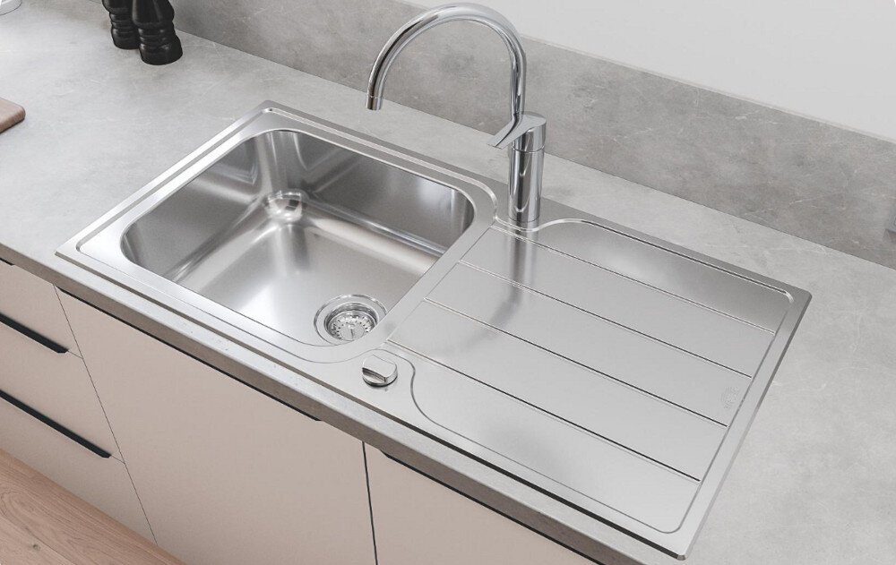 Zlewozmywak jednokomorowy z ociekaczem GROHE K500 31563SD1 Stal szlachetna Na zdjęciu widać stalowy zlewozmywak jednokomorowy z ociekaczem, osadzony w blacie o ciemnoszarej powierzchni. W centralnej części ociekacza znajduje się chromowana, jednouchwytowa bateria stojąca, a w tle widoczne są minimalistyczne akcesoria kuchenne na białej półce.