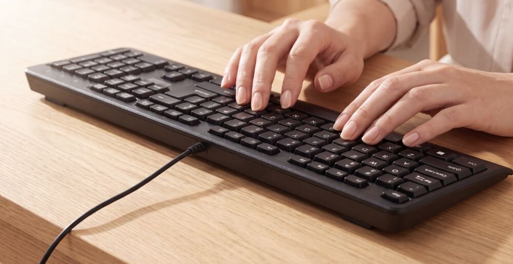 LENOVO 160 Wired Combo Klawiatura pełnowymiarowy układ klawiaturą numeryczną diody Num Lock, Caps Lock i Scroll Lock - Dłonie opierające się na czarnej klawiaturze przewodowej, gotowe do pisania, na powierzchni drewnianego biurka