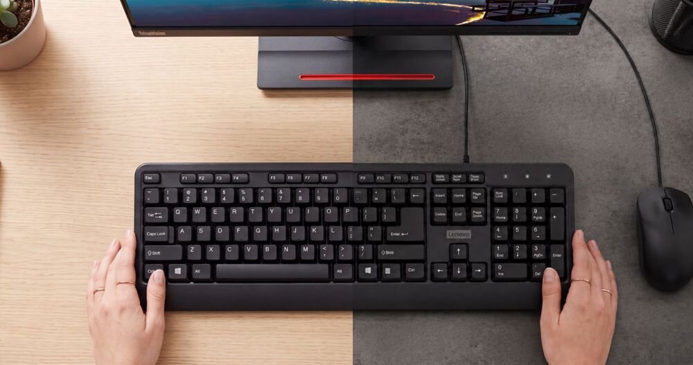 LENOVO 160 Wired Combo Klawiatura 524 g mysz 93 g Niska masa wygodnie zabrać je ze sobą - Porównawczy widok z góry na klawiaturę z dłońmi na podzielonym tle blatu drewnianego i ciemnoszarego