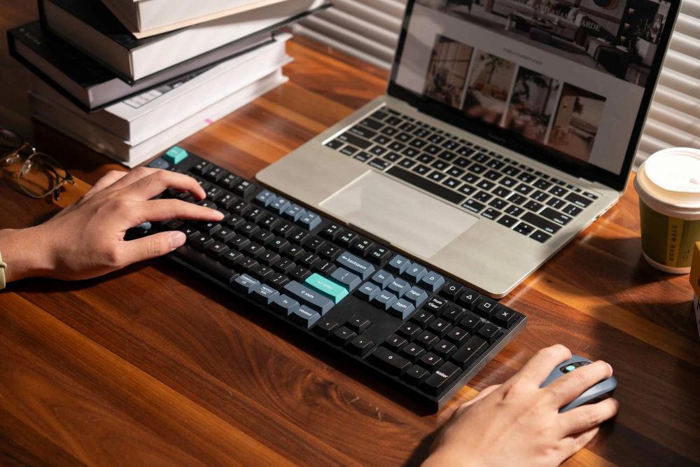 Zestaw KEYCHRON Wireless Combo KCBD2 Mysz BM25 przyciski boczne lewej stronie obudowy użytkowników praworęcznych dodatkowych funkcji kciukiem - ręce na zestawie na biurku obok laptopa