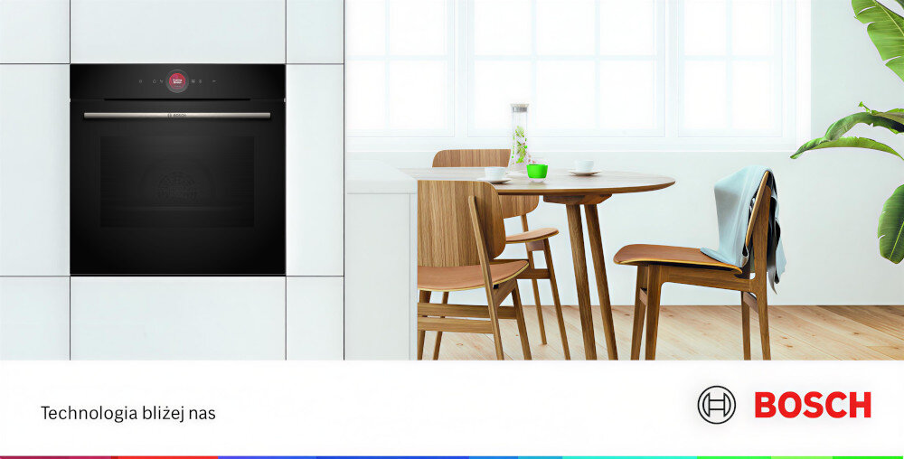 PIEKARNIK BOSCH HBG7242BB1 Piekarnik w zabudowie znajduje się obok drewnianego stołu ustawionego przy dużych oknach, które wpuszczają naturalne światło. Na dole dodano hasło „Technologia bliżej nas” wraz z logo marki Bosch