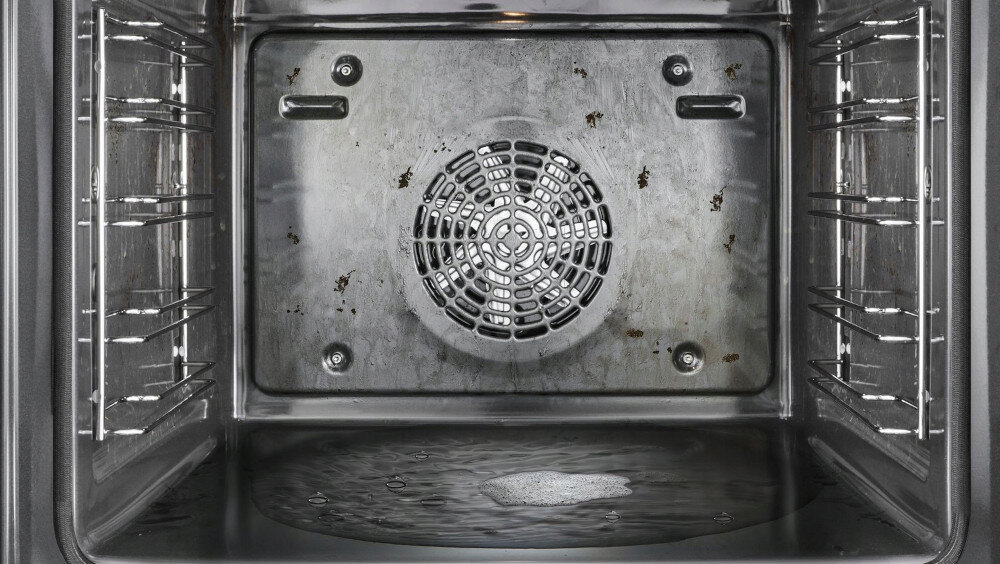 PIEKARNIK BOSCH HBG7242BB1 Wnętrze piekarnika pokazuje metalową komorę z wentylatorem na tylnej ściance oraz śladami po zabrudzeniach. Na dnie znajduje się warstwa wody i piana, co sugeruje działanie funkcji czyszczenia parowego Asystent czyszczenia szybkie czyszczenie woda zmiękczanie zabrudzeń