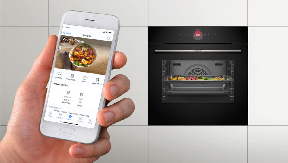 PIEKARNIK BOSCH HBG7242BB1 Ręka trzyma smartfon z otwartą aplikacją kulinarną, a obok widać piekarnik z potrawą piekącą się na dwóch poziomach. Kompozycja podkreśla możliwość sterowania urządzeniem i korzystania z przepisów z poziomu telefonu Home Connect zdalne sterowanie piekarnikiem głos Alexa Google powiadomienia aktualizacje