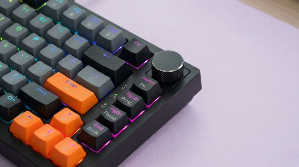 Klawiatura mechaniczna z czarno-szaro-pomarańczowymi klawiszami i podświetleniem RGB. Widoczny jest także duży, czarny pokrętło w prawym górnym rogu.