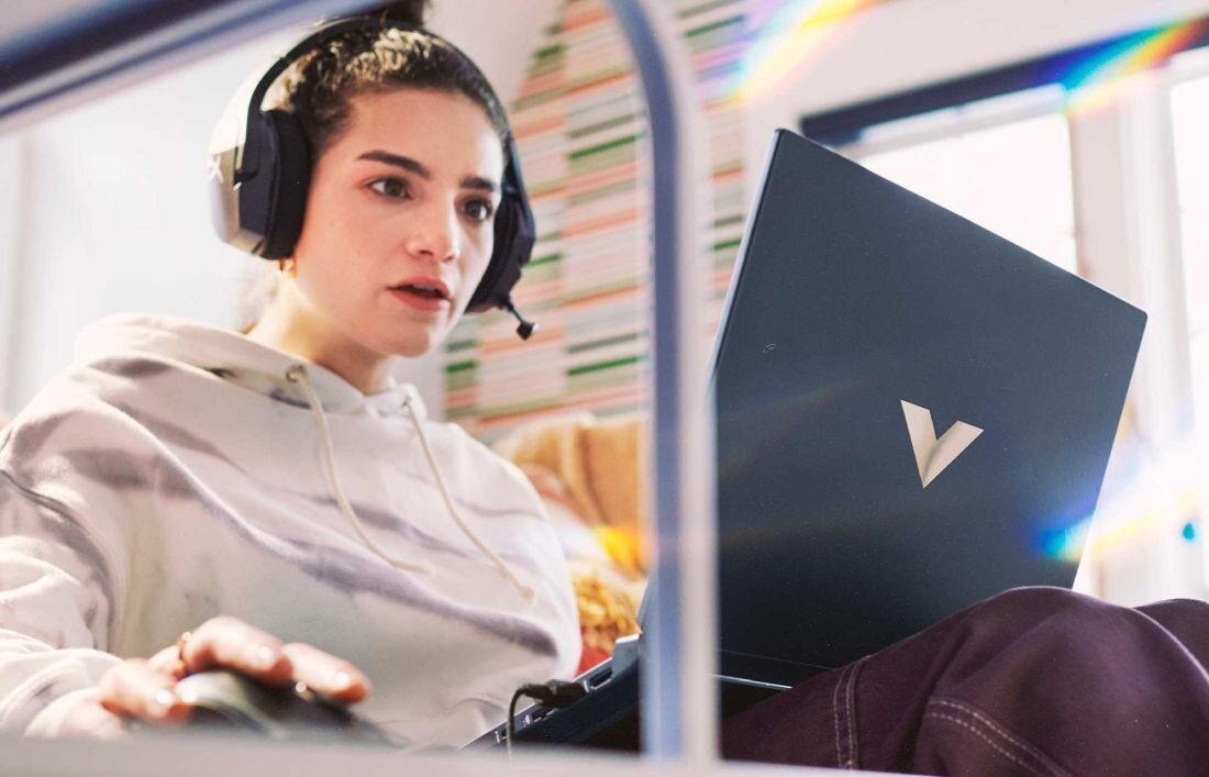 Laptop HP Victus 15 - Kobieta w białej bluzie i słuchawkach siedzi w autobusie z laptopem, skupiona na pracy lub relaksie. Ekologia w technologii 