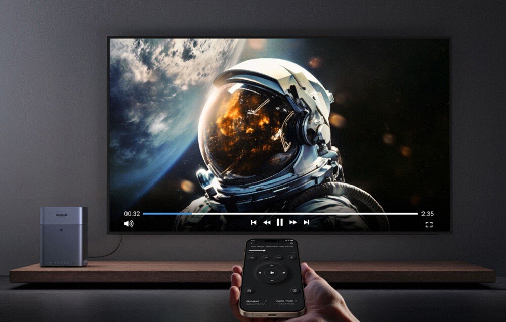 Na obrazie widoczny jest duży ekran telewizora, na którym wyświetlany jest film z astronautą w kosmosie. Obok telewizora znajduje się urządzenie z logo \'media expert\', a na pierwszym planie widoczny jest pilot zdalnego sterowania.