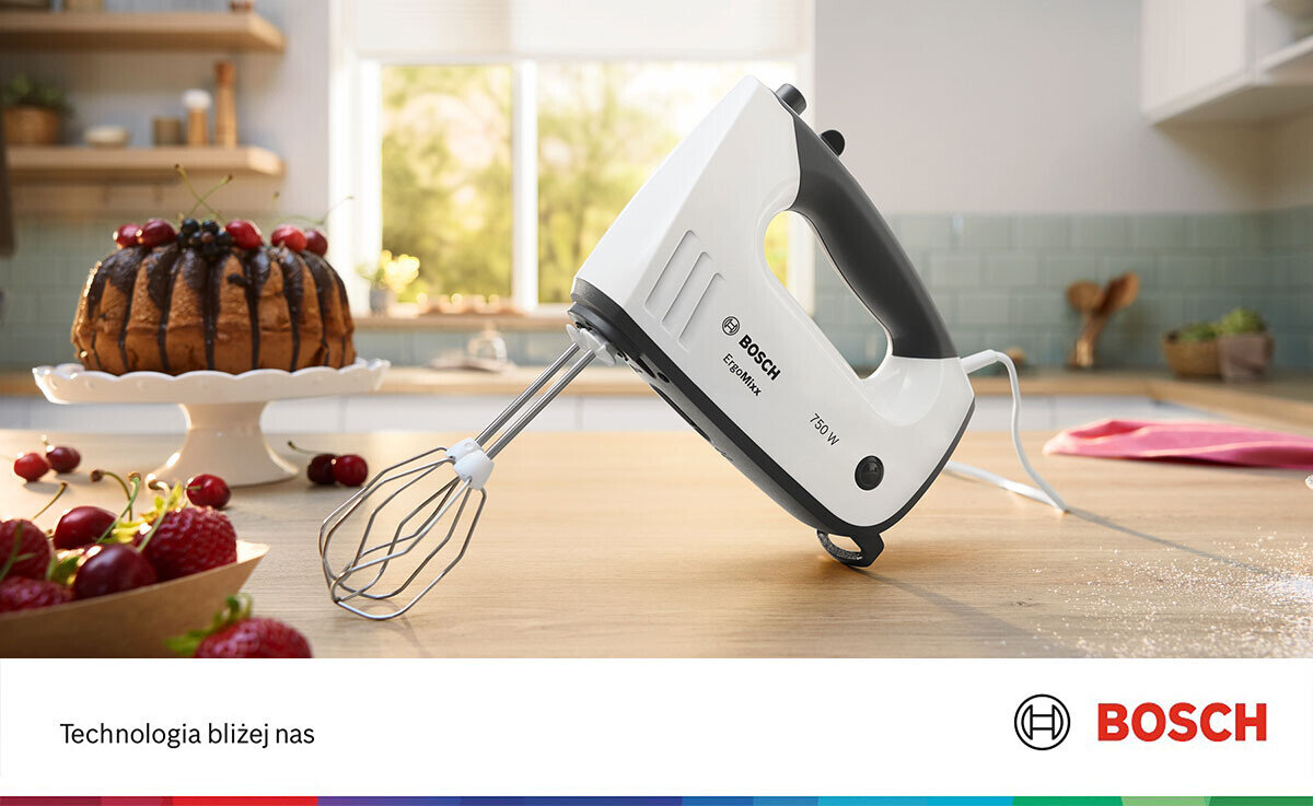 Na blacie kuchennym stoi biały mikser ręczny z logo BOSCH i napisem \'750 W\'. W tle widoczny jest ciasto na paterze oraz owoce, a na dole obrazu znajduje się napis \'Technologia bliżej nas\' i logo BOSCH.