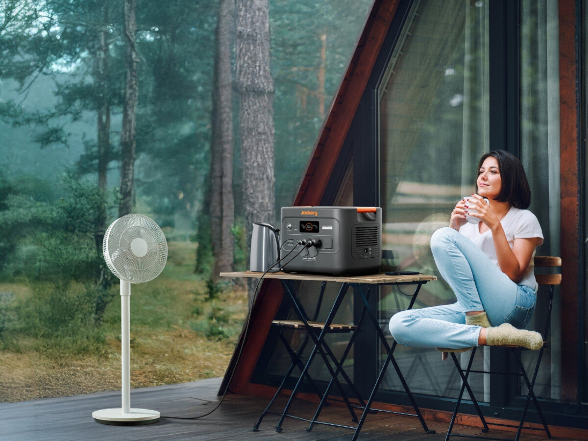 Stacja zasilania JACKERY Explorer 3000 V2 EU 3072 Wh Bank energii, lekka, 27kg, kółka, CTB, kobieta w domku leśnym siedzi na krzesełku, obok wentylator zasilany stacją zasilania
