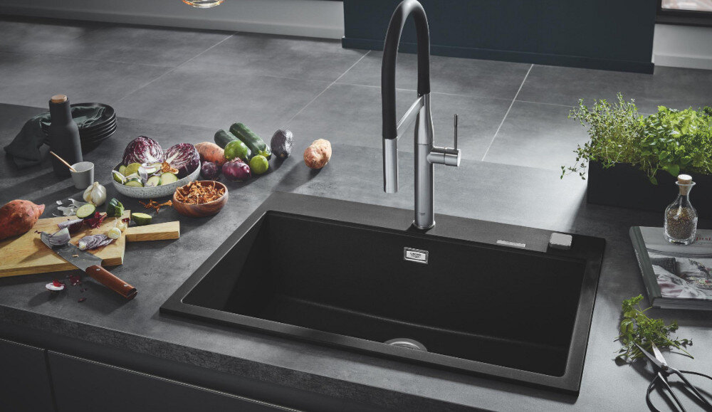 Zlewozmywak jednokomorowy GROHE K700 80-C 78/51 1.0 31652AP0 Czarny jednokomorowy zlewozmywak wpuszczany w blat z wysoką, chromowaną baterią kuchenną. Wokół stoją produkty spożywcze i dodatki kuchenne tworzące estetyczną aranżację
