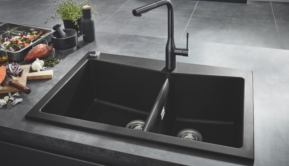Zlewozmywak dwukomorowy GROHE K700 90-C 83.8/55.9 2.0 31657AP0 Czarny dwukomorowy zlewozmywak wpuszczany w blat z wysoką, chromowaną baterią kuchenną. Wokół stoją produkty spożywcze i dodatki kuchenne tworzące estetyczną aranżację