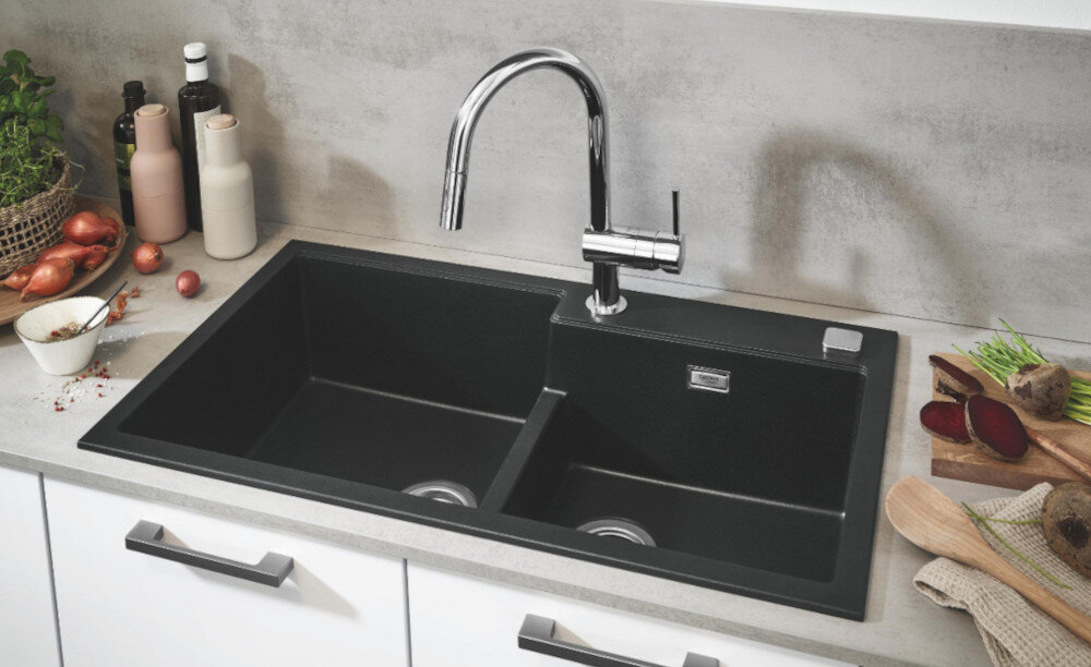 Zlewozmywak dwukomorowy GROHE K500 90-C 86/50 2.0 31649AP0 Czarny dwukomorowy zlewozmywak wpuszczany w blat z wysoką, chromowaną baterią kuchenną. Wokół stoją produkty spożywcze i dodatki kuchenne tworzące estetyczną aranżację
