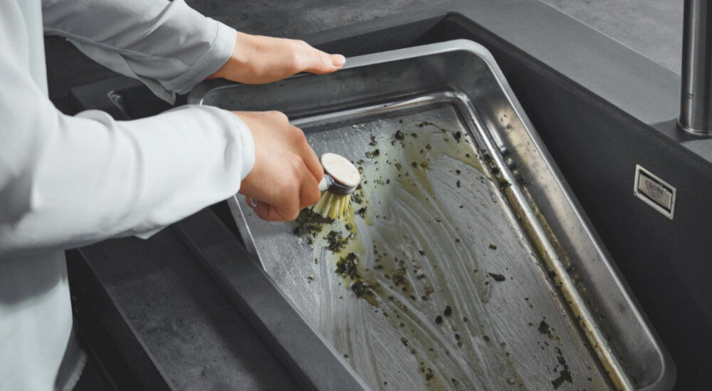 Zlewozmywak dwukomorowy GROHE K500 90-C 86/50 2.0 31649AP0 W dużej stalowej blasze w zlewie ktoś myje naczynie przy użyciu szczotki. Scena podkreśla funkcjonalność głębokiej komory zlewu zlewozmywak dwukomorowy GROHE funkcjonalność porządek wygoda kuchnia mycie płukanie