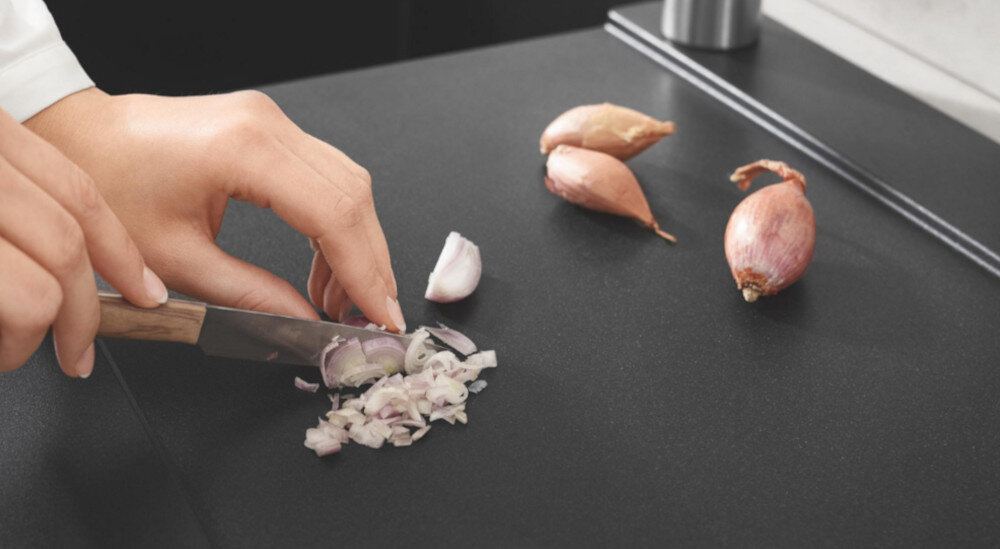 Zlewozmywak dwukomorowy GROHE K500 90-C 86/50 2.0 31649AP0 Na blacie przy zlewie krojone są cebulki szalotki ostrym nożem. Zdjęcie podkreśla odporność powierzchni na zarysowania podczas codziennego użytkowania kwarc trwałość wytrzymałość odporność na uszkodzenia