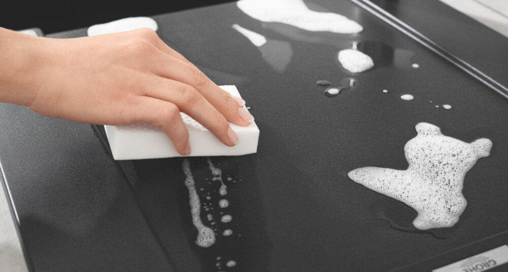 Zlewozmywak dwukomorowy GROHE K500 90-C 86/50 2.0 31649AP0 Ręka przeciera gąbką czarną powierzchnię ociekacza z pianą. Ujęcie akcentuje gładką strukturę i łatwe czyszczenie dla zachowania eleganckiego wyglądu łatwe czyszczenie gładka powierzchnia odporność UV elegancki wygląd