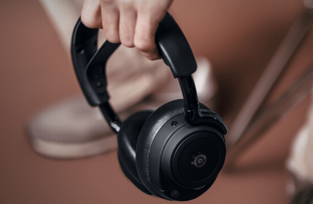 Słuchawki STEELSERIES Arctis Nova Elite Infinite Power System akumulator 700mAh GameHub, osoba trzymająca słuchawki w ręku