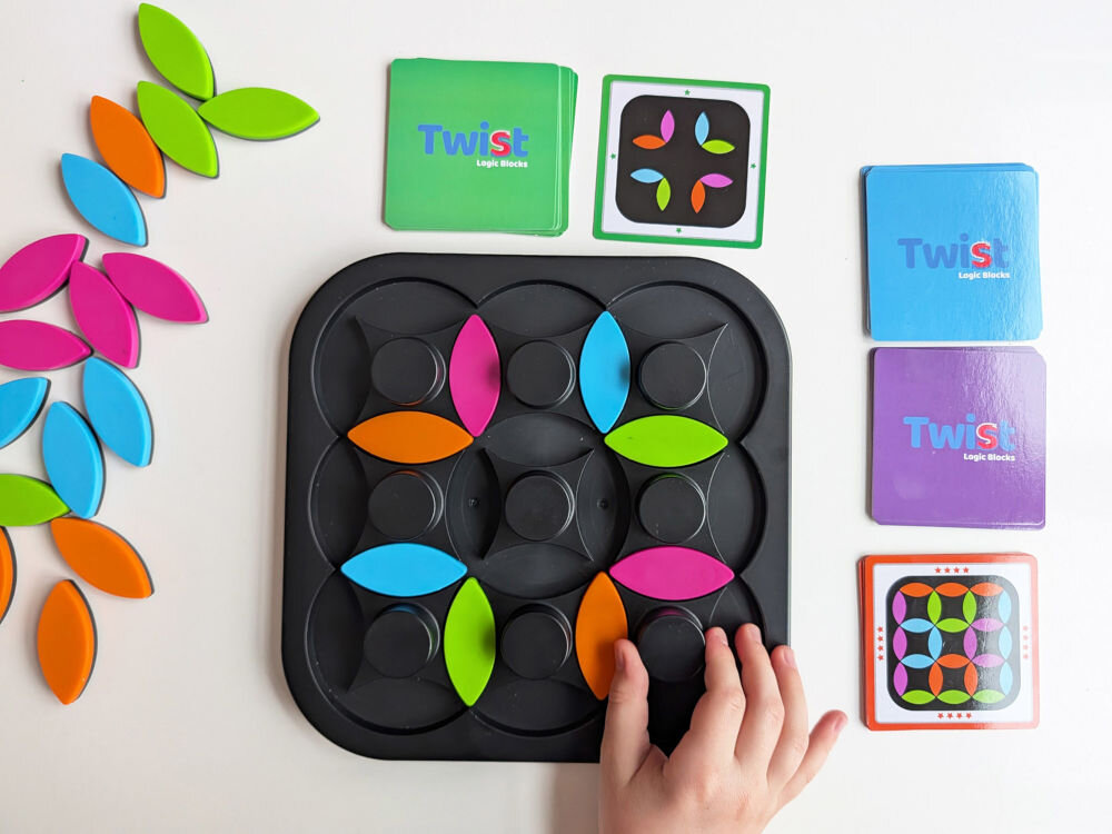 Gra logiczna ASKATO Genialny dzieciak Twist Kręć z głową 127651 Wielokolorowy Gra logiczna Twist Logic Blocks z ułożonymi płatkami na planszy, kartami zadań oraz stosem kolorowych elementów obok.