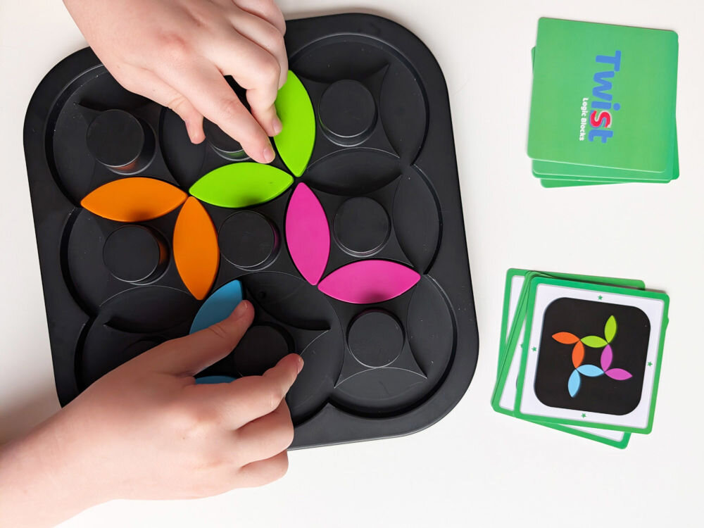 Gra logiczna ASKATO Genialny dzieciak Twist Kręć z głową 127651Dłonie dziecka układające kolorowe elementy łamigłówki Twist Logic Blocks zgodnie ze wzorem na karcie zadania.