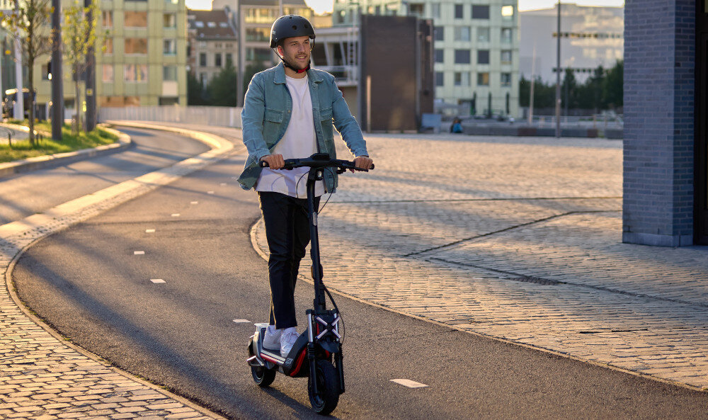 Hulajnoga elektryczna SEGWAY Ninebot ZT3 Pro D 70km 1600W Amortyzacja 11 cali Czarny hulajnoga miasto osoba jedzie po drodze na hulajnodze w tle budynki chodnik 3 tryby jazdy tryb pieszy prędkość do 6 km/h tryb ECO prędkość do 15 km/h tryb SPORT prędkość do 20 km/h