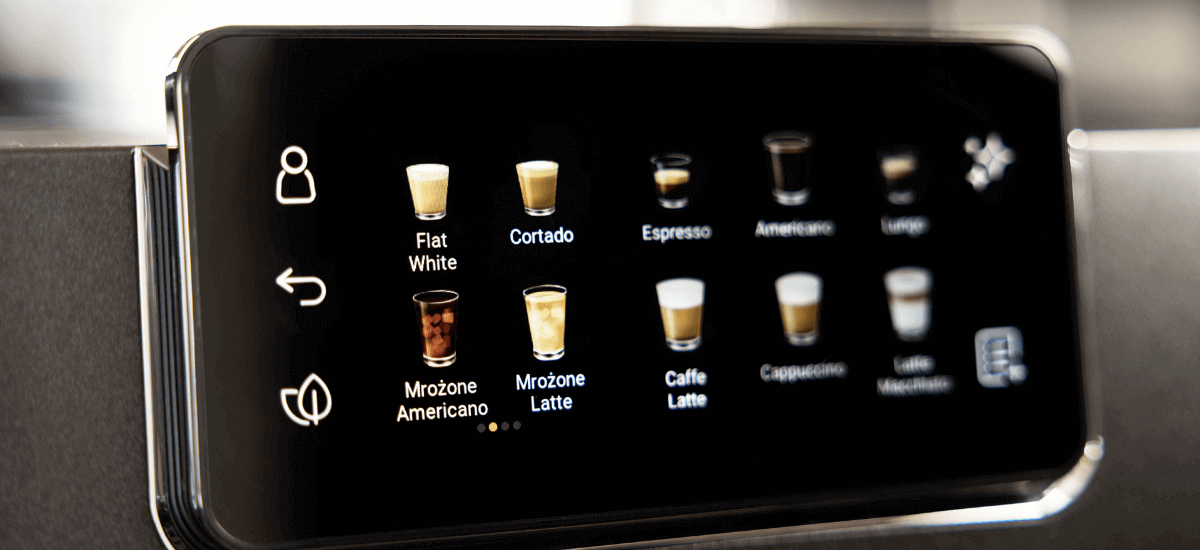 Wyświetlacz ekspresu do kawy pokazuje różne opcje napojów, takie jak Flat White, Cortado, Espresso, Americano, Lungo, Mrożone Americano, Mrożone Latte, Caffe Latte, Cappuccino i Latte Macchiato.