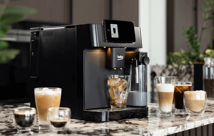 Czarny ekspres do kawy z logo \'beko\' na blacie kuchennym, obok kilka szklanek z różnymi rodzajami kawy, w tym kawa z lodem. Na ekspresie widoczny jest ekran z grafiką filiżanki kawy.