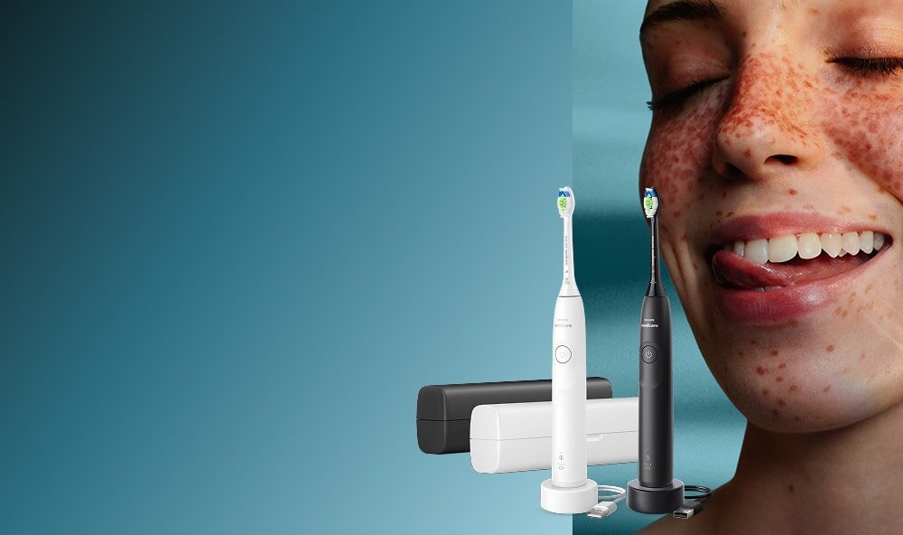 Zbliżenie na twarz uśmiechniętej kobiety, która językiem przesuwa po zębach. Obok zestaw szczoteczek sonicznych z etui.