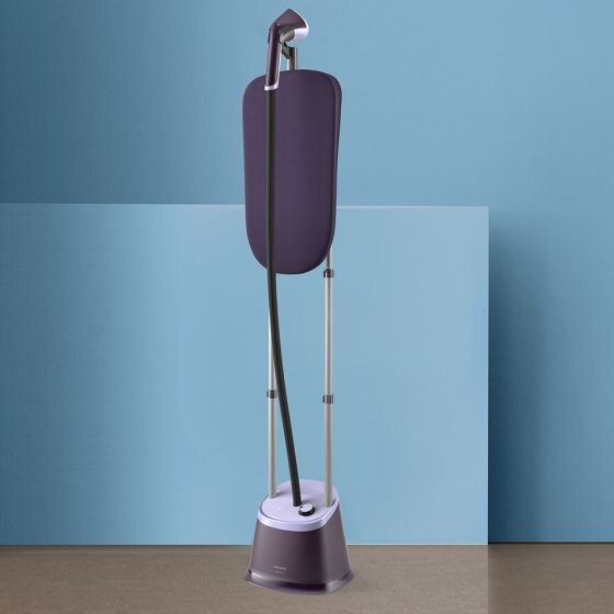 Na obrazie znajduje się parownica do ubrań w kolorze fioletowym z długim wężem i stojakiem. W tle widoczna jest niebieska ściana.