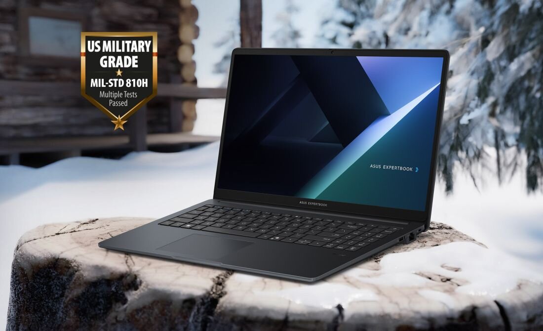 Laptop ASUS ExpertBook stoi na drewnianym pniu w zimowym otoczeniu. Obok widoczna jest odznaka z napisem \'US MILITARY GRADE MIL-STD 810H Multiple Tests Passed\'.