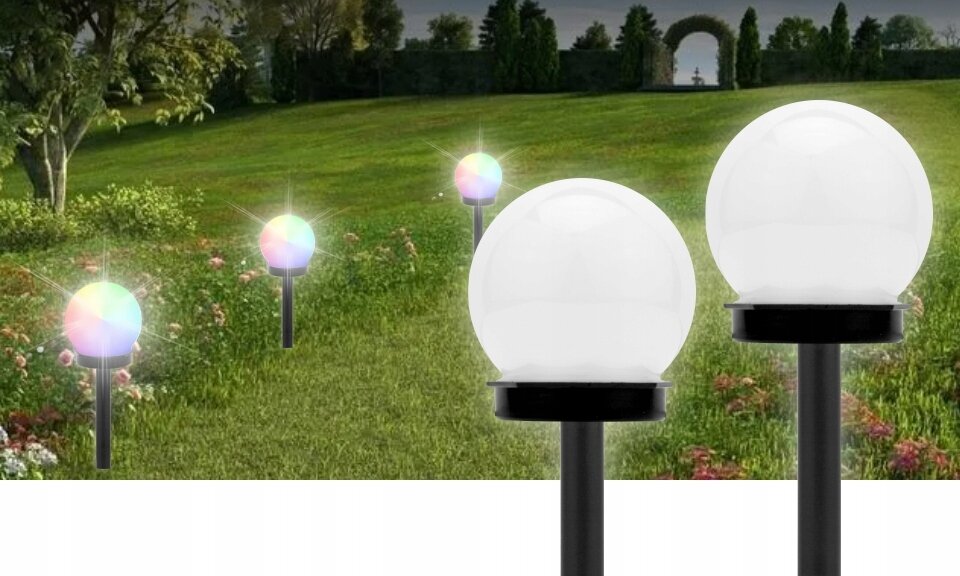 Na obrazie widać kilka kulistych lamp solarnych umieszczonych na trawniku, emitujących kolorowe światło. W tle znajduje się zieleń i drzewa.