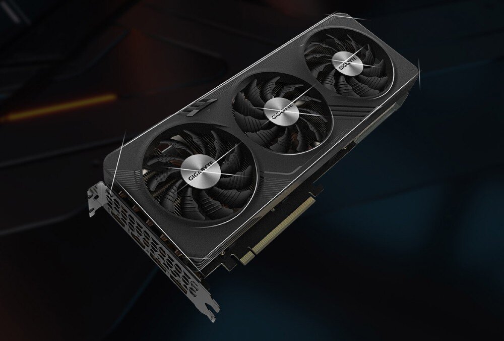 Karta graficzna GIGABYTE Radeon RX 7600 XT Gaming OC 16GB Skośny widok karty graficznej z trzema wentylatorami i metalową osłoną, umieszczonej na ciemnym tle, głośność, tryb półpasywny