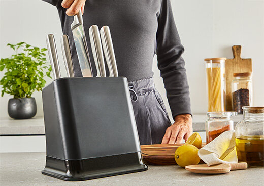 Osoba wyciąga jeden z noży K2977S44 czarnego bloku na noże kuchenne. Na kuchennym blacie obok znajdują się przyprawy.