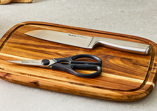 Nóż kuchenny K2977S44 i nożyce Tefal EverSharp ułożone na drewnianej desce do krojenia.