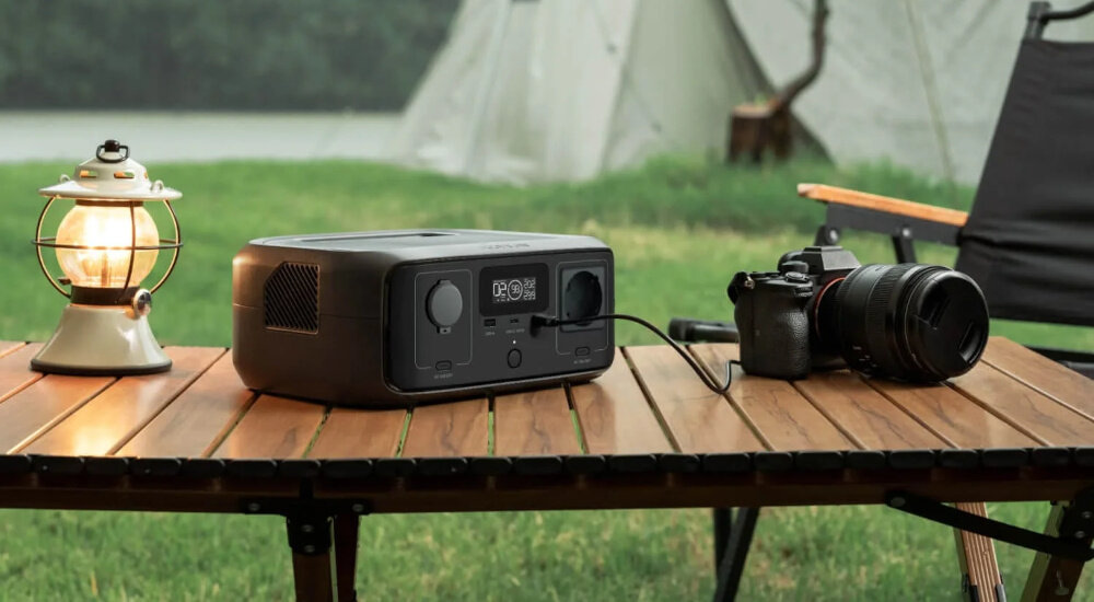 Stacja zasilania ECOFLOW River 3 Plus 286 Wh stacja stoi na stoliku obok aparat i lampka kempingowa w tle namiot i trawa tle dodatkowe źródło energii duża wydajność energia w razie awarii