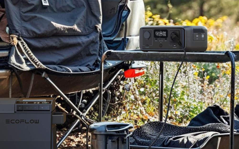 Stacja zasilania ECOFLOW River 3 Plus 286 Wh stacja stoi na stoliku kempingowym obok krzesło kempingowe w tle bagażnik samochodowy rozszerzalna pojemność moc wyjściowa do 600 W tryb X-Boost do 1200 W półprzewodnik generacji GaN azotek galu wyższa wydajność energetyczna niższe straty ciepła lekka wytrzymała konstrukcja stałe źródło zasilania